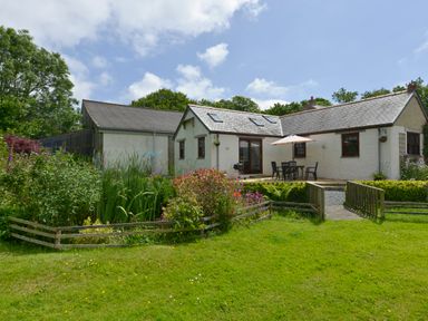 An outdoor view of a white house with a patio table and umbrella surrounded by garden and grass at Valley View in St Martin near Mawgan