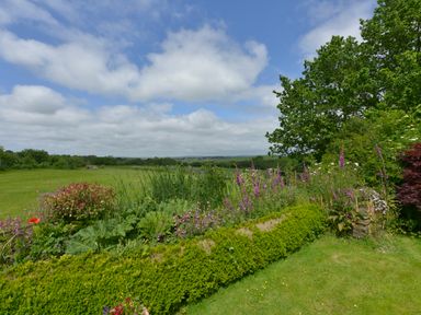 A garden with flowering plants trees and grass under a partly cloudy sky at Valley View in St Martin near Mawgan