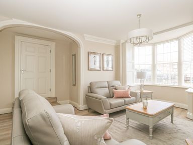 A living room with grey sofas a wooden coffee table a side table with a lamp and large windows at Harbour Watch 2 in Weymouth