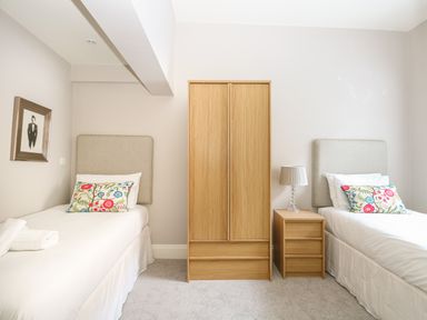 A bedroom with two single beds a wooden wardrobe and a wooden bedside table with a lamp at Harbour Watch 2 in Weymouth