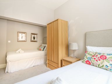 A bedroom with two single beds a wooden wardrobe a bedside table and a lamp at Harbour Watch 2 in Weymouth