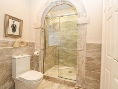 A bathroom with a toilet shower area with glass doors and stone archway at Harbour Watch 2 in Weymouth