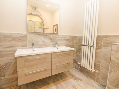 A bathroom with a double sink vanity a large mirror beige tiled walls and floor and a tall white radiator at Harbour Watch 2 in Weymouth