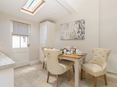 A kitchen dining area with a wooden table set with cups and fruit a door a skylight and light colored chairs at Harbour Watch 2 in Weymouth