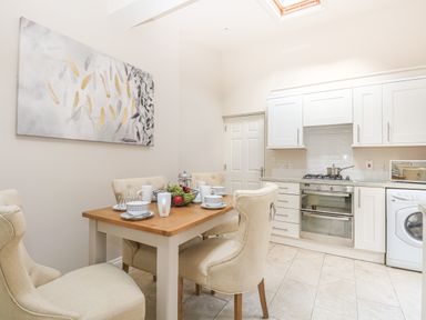 A kitchen with a dining table set with cups and bowls beige chairs white cabinets and a washing machine at Harbour Watch 2 in Weymouth