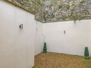 An outdoor area with white walls a stone wall section gravel ground and two small potted plants at Harbour Watch 2 in Weymouth