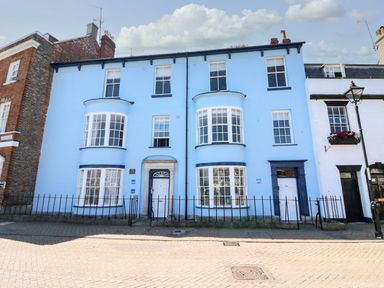 A street view of a blue painted building with white framed windows and two white doors in a row of attached houses