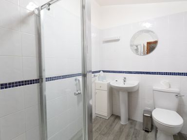A bathroom with a shower, sink, toilet, round mirror, and a small cabinet at Riverhouse Lodge in Upwey