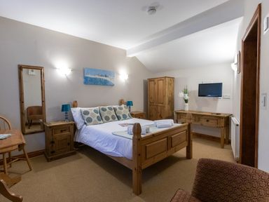 A bedroom with a wooden bed and side tables a wooden wardrobe a desk with a vase a wall-mounted TV and a chair at Riverhouse Lodge in Upwey