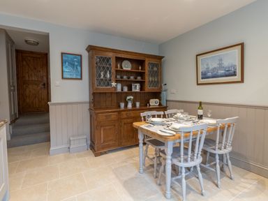 A dining area with a wooden dining table set with plates and glasses and a wooden cabinet with dishes and decorations in Riverhouse Lodge Upwey