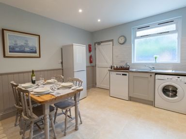 A kitchen with a dining table set for four a refrigerator dishwasher washing machine and a window at Riverhouse Lodge in Upwey