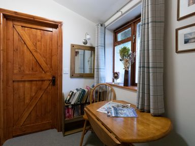A small room with a wooden table and chair near a window with curtains and a wooden door at Riverhouse Lodge in Upwey