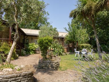 A garden with a gravel path shrubs trees and outdoor chairs and table at Riverhouse Lodge in Upwey