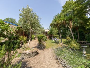 An outdoor garden with a gravel path trees shrubs and plastic chairs at Riverhouse Lodge in Upwey