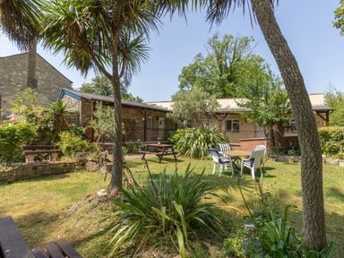 A garden with tables and chairs surrounded by trees and plants at Riverhouse Lodge in Upwey