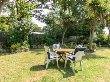 A garden with a wooden table and four white chairs with striped cushions at Riverhouse Lodge in Upwey
