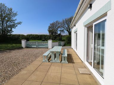 An outdoor patio with a wooden picnic table and benches next to a white house at Yr Hen Ardd in Dale near Milford Haven
