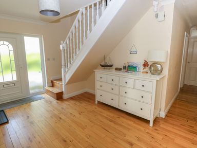 An entrance hallway with wooden flooring a white staircase a white chest of drawers with a lamp and model boat at Yr Hen Ardd Dale near Milford Haven