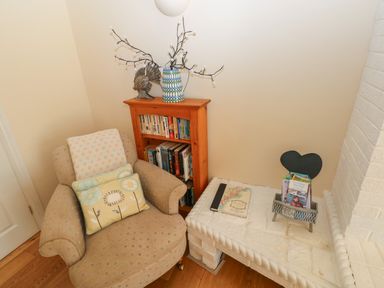 A corner with an armchair next to a wooden bookshelf and a white brick hearth with books at Yr Hen Ardd in Dale near Milford Haven