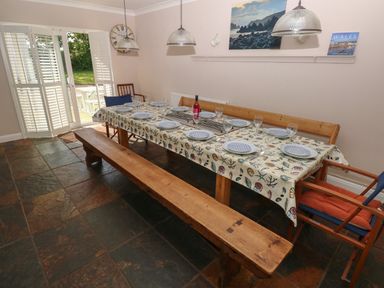 A dining room with a long wooden table set with plates and glasses wooden benches and chairs with sliding doors leading outside at Yr Hen Ardd in Dale near Milford Haven