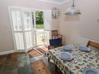 A dining area with a table set with plates and glasses a wooden bench and chair near glass doors with shutters at Yr Hen Ardd in Dale near Milford Haven