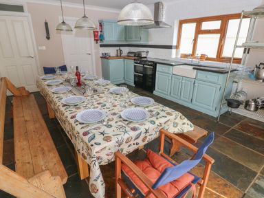 A kitchen with a dining table set with plates and glasses blue cabinets and wooden benches at Yr Hen Ardd in Dale near Milford Haven