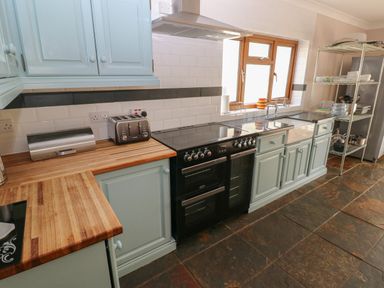 A kitchen with wooden countertops a black stove and oven blue cabinets a stainless steel bread box toaster and a metal shelving unit at Yr Hen Ardd in Dale near Milford Haven