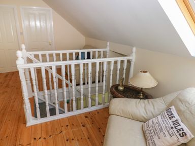An upstairs landing with wooden floors a white staircase railing beige sofas a side table with a lamp and cushion at Yr Hen Ardd in Dale near Milford Haven