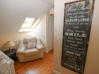 A corner with a beige armchair pillow side table lamp skylight window and a wall sign with house rules at Yr Hen Ardd Dale near Milford Haven