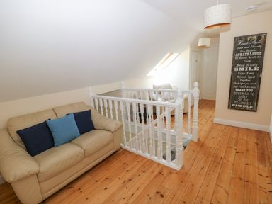 A sitting area with a beige sofa with cushions near a white staircase railing and a wooden floor at Yr Hen Ardd in Dale near Milford Haven
