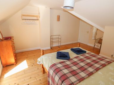 A bedroom with a wooden bed with folded towels and a blanket a wooden chest of drawers a chair and a door at Yr Hen Ardd in Dale near Milford Haven