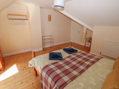 A bedroom with a bed, folded towels, a wall-mounted hanger with hangers, a chair with a cushion, and a radiator at Yr Hen Ardd in Dale near Milford Haven