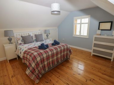 A bedroom with a double bed cushions bedside tables lamps a window and a chest of drawers at Yr Hen Ardd in Dale near Milford Haven