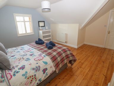 A bedroom with a bed with floral bedding and plaid blanket and a chest of drawers under a window at Yr Hen Ardd in Dale near Milford Haven
