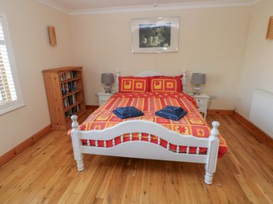 A bedroom with a white bed frame and colorful bedspread with two folded towels on the bed at Yr Hen Ardd in Dale near Milford Haven