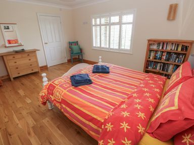 A bedroom with a double bed with patterned bedding a wooden chest of drawers a wooden bookshelf and a chair at Yr Hen Ardd in Dale near Milford Haven
