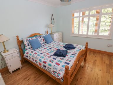 A bedroom with a wooden bed with patterned bedding two blue pillows two folded towels and bedside tables with lamps at Yr Hen Ardd in Dale near Milford Haven