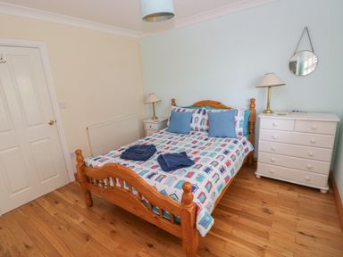 A bedroom with a wooden bed two bedside tables with lamps a white chest of drawers and a round wall mirror at Yr Hen Ardd in Dale near Milford Haven