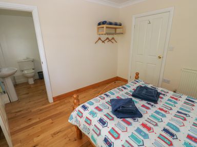 A bedroom with a wooden bed covered with a patterned duvet and towels on top a door a shelf with hangers and an open door leading to a bathroom at Yr Hen Ardd in Dale near Milford Haven