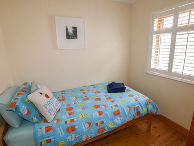 A small bedroom with a single bed a colorful bedspread a pillow that says pretty please and a window with white shutters at Yr Hen Ardd in Dale near Milford Haven