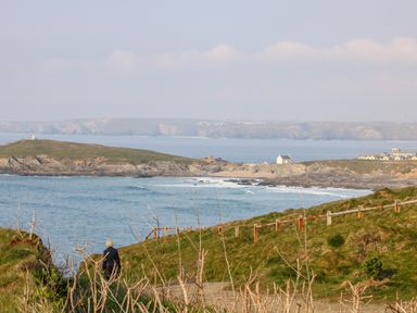 A person walking on a coastal path overlooking the sea grassy hills and distant buildings at 8 Cribbar in Newquay