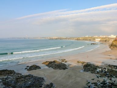 A beach with waves and rocks with people on the sand and distant buildings at 8 Cribbar in Newquay