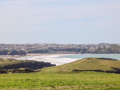 A coastal landscape with grassy cliffs overlooking a beach and a town in the distance at 8 Cribbar in Newquay