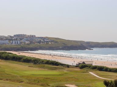 A beach with people by the ocean and a grassy area with a golf course near buildings on a hill at 8 Cribbar in Newquay