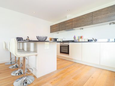 A modern kitchen with white cabinets and bar stools at 8 Cribbar in Newquay