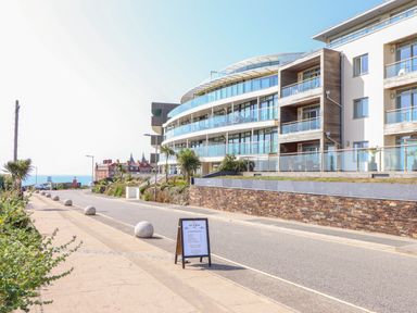 A street with a modern building with balconies and a signboard on the sidewalk near the sea at 8 Cribbar in Newquay