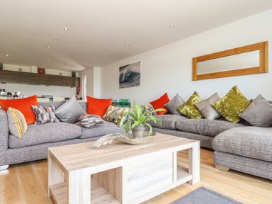 A living room with grey sofas with colorful cushions and a wooden coffee table with a plant at 8 Cribbar in Newquay