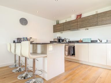 A kitchen with four white bar stools a countertop wooden floor and wall cabinets at 8 Cribbar in Newquay