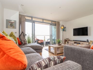 A living room with two gray sofas a wooden coffee table a flat screen tv and glass doors leading to a balcony at 8 Cribbar in Newquay