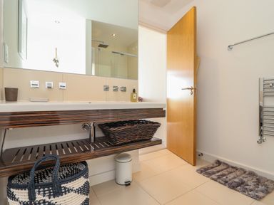 A bathroom with a wooden door open showing a double sink with a large mirror above it and woven baskets below at 8 Cribbar in Newquay